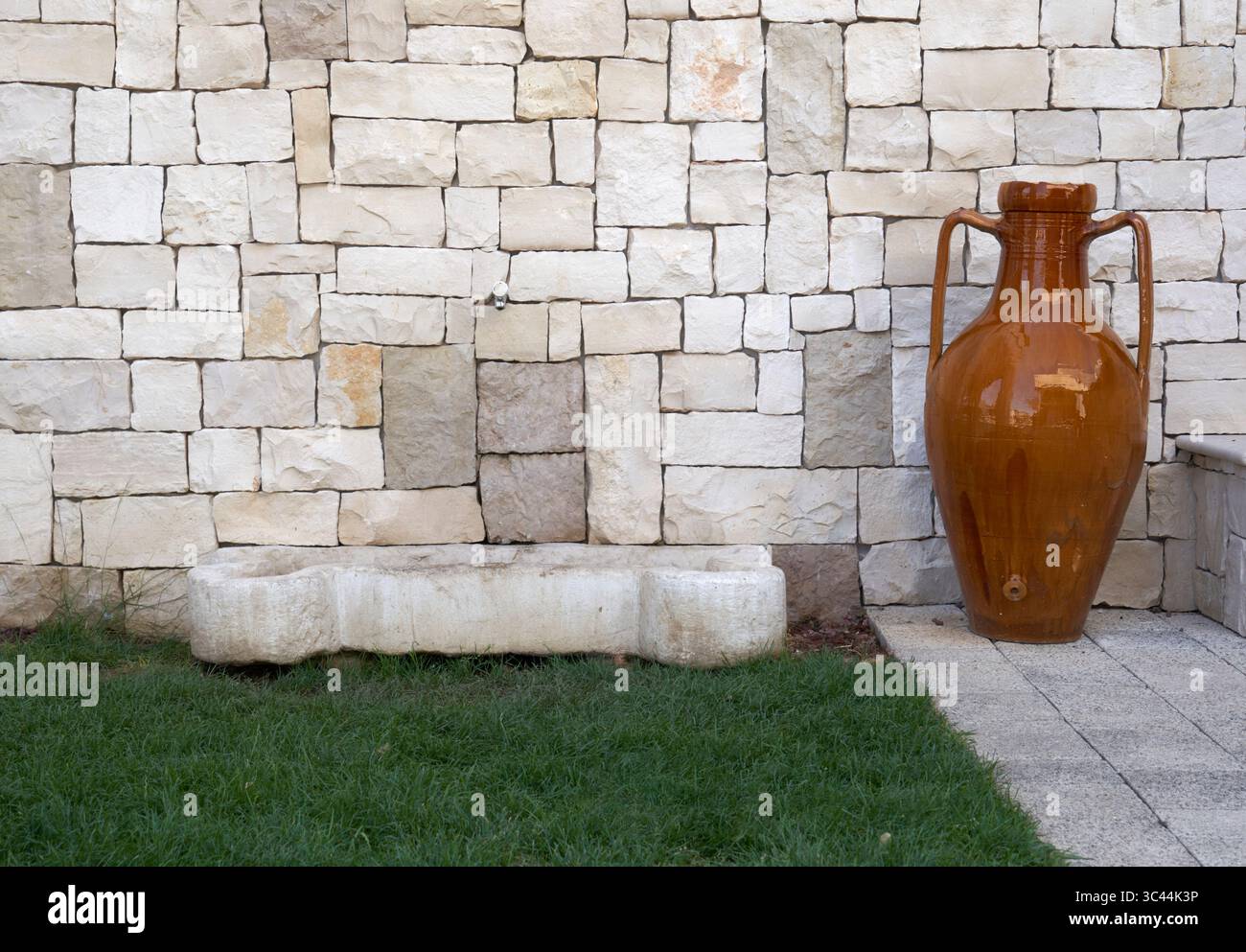 Fontaine murale traditionnelle en pierre agrémentée d'amphores en céramique vintage, située sur l'herbe dans un jardin de style méditerranéen. Banque D'Images