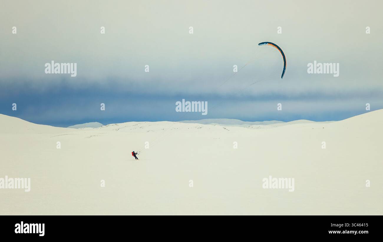 Hardangervidda, Norvège - 21 mars 2024 : une personne faisant du snowkite à travers le vaste plateau de montagne enneigé sous un ciel nuageux en Scandinavie. Banque D'Images