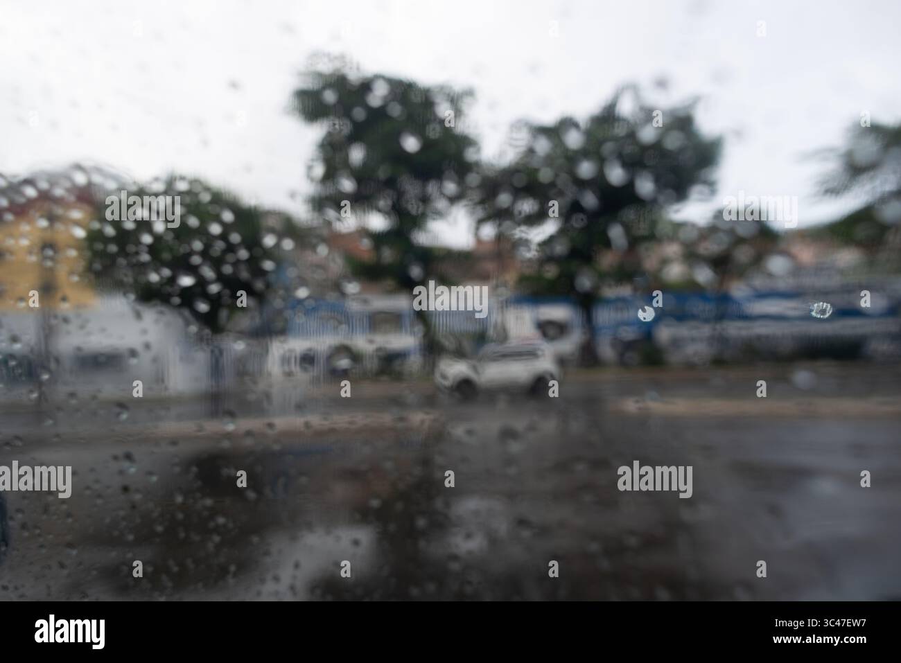 Vue floue avec des gouttes de pluie sur le verre d'une voiture dans une rue pendant le mouvement de la circulation. Texture. Arrière-plan Banque D'Images