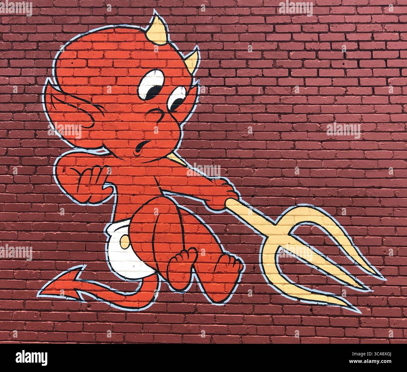 Le Street art ludique à Asheville, en Caroline du Nord, montre un bébé diable espiègle dans des couches, souriant grand et indiquant le chemin de l'enfer. Banque D'Images