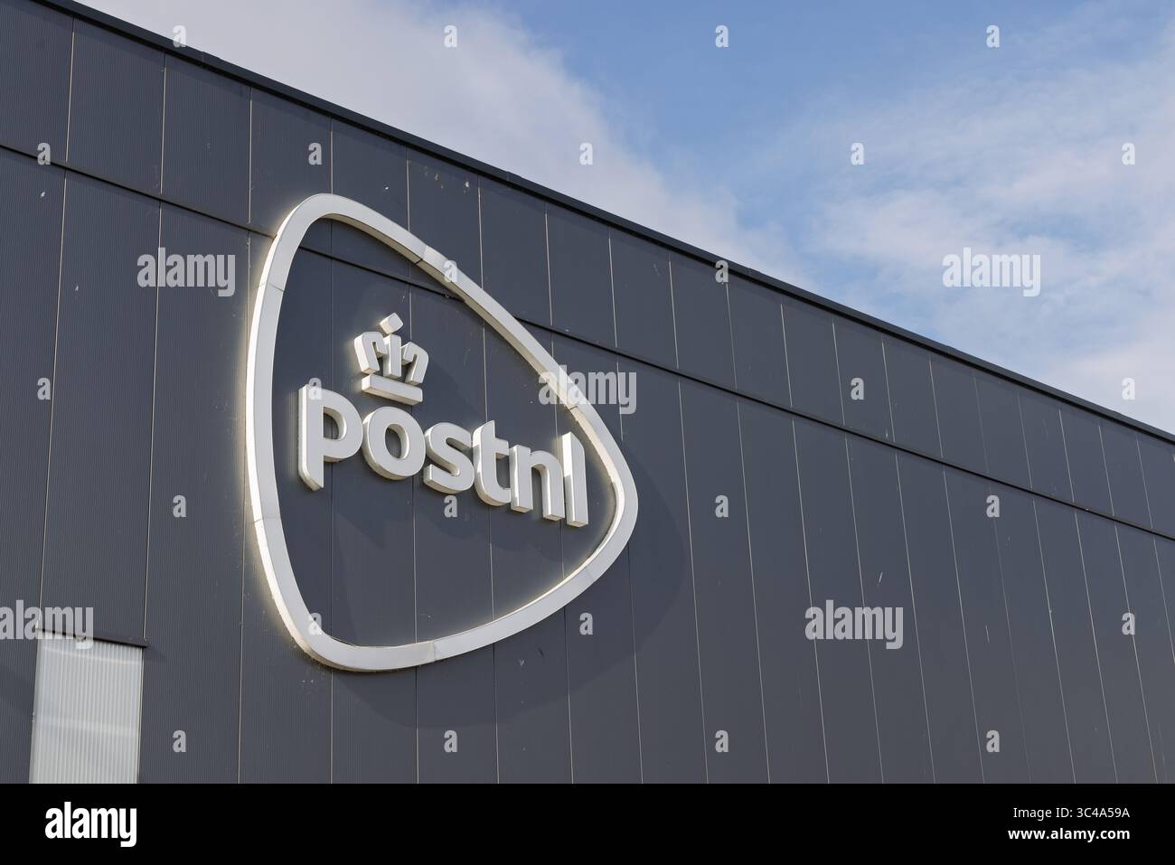 Le logo proéminent de PostNL, avec une couronne et le nom de l'entreprise, est monté sur l'extérieur gris foncé, lambrissé verticalement d'un bâtiment moderne sous le toit Banque D'Images