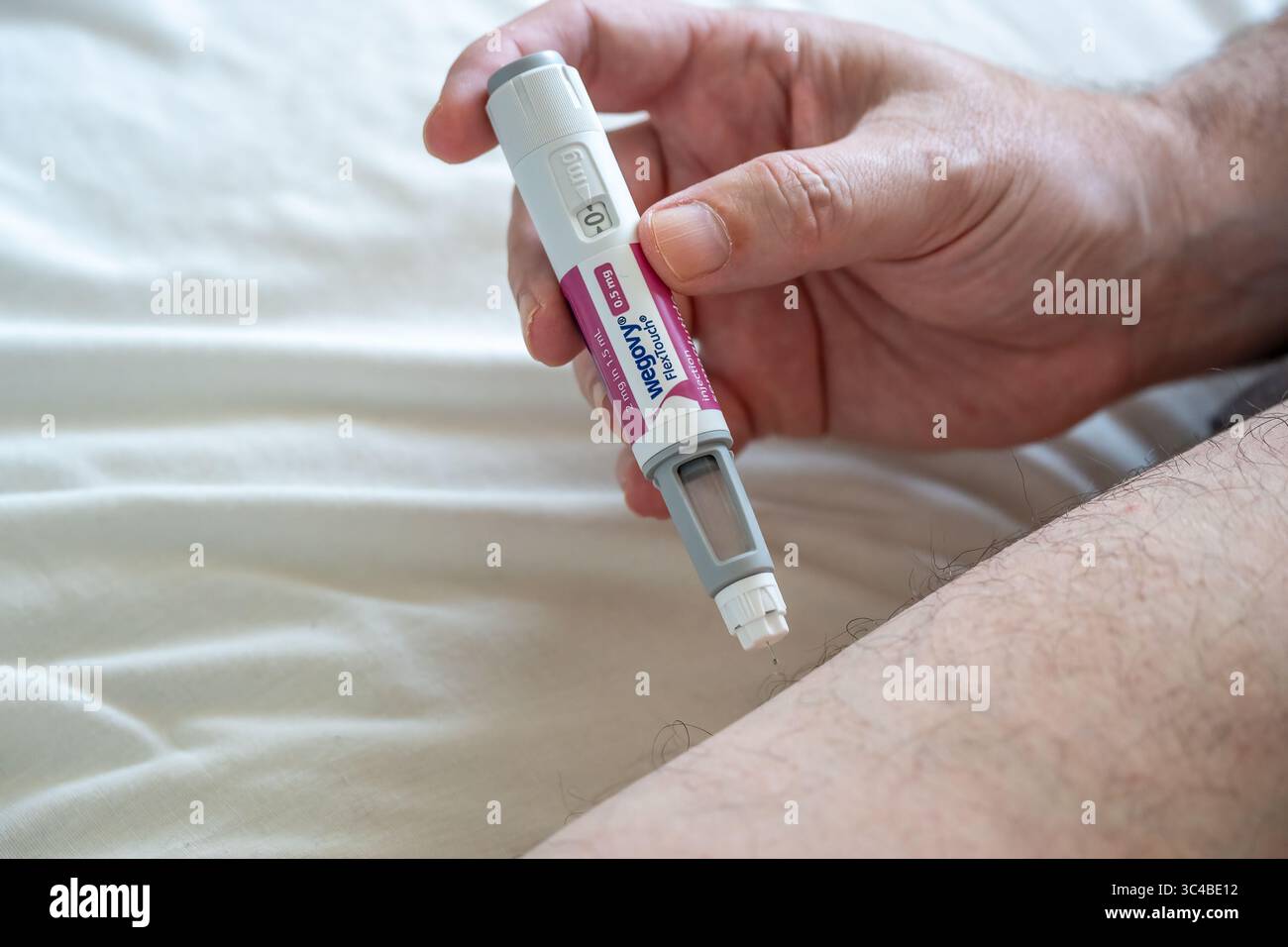 Homme utilisant un stylo injectable Wegovy pour le traitement de perte de poids, en administrant une dose sous-cutanée dans la cuisse. Concept de prise en charge de l'obésité et de la santé. Banque D'Images