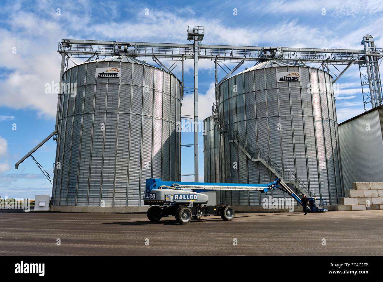 23 juillet 2025 – Ystad-Suède : deux silos à grains de marque Almas et un ascenseur de rampe Rallco se tiennent sur de l’asphalte fraîchement pavé dans une zone agricole et de construction Banque D'Images