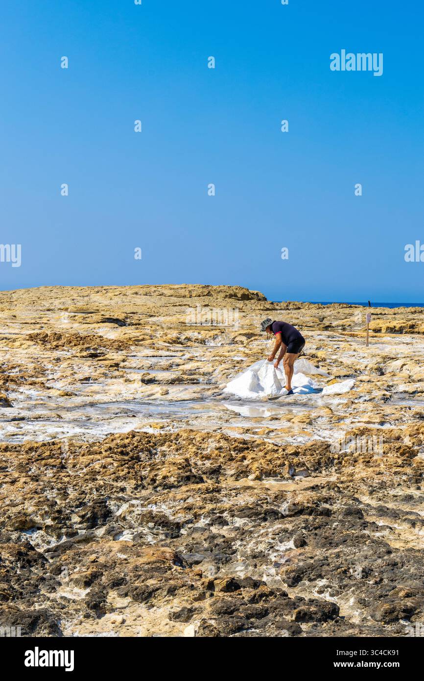 Homme recueillant le sel de mer naturel des marais salants au spot de plongée de Ras il Hobz, Gozo, Malte Banque D'Images