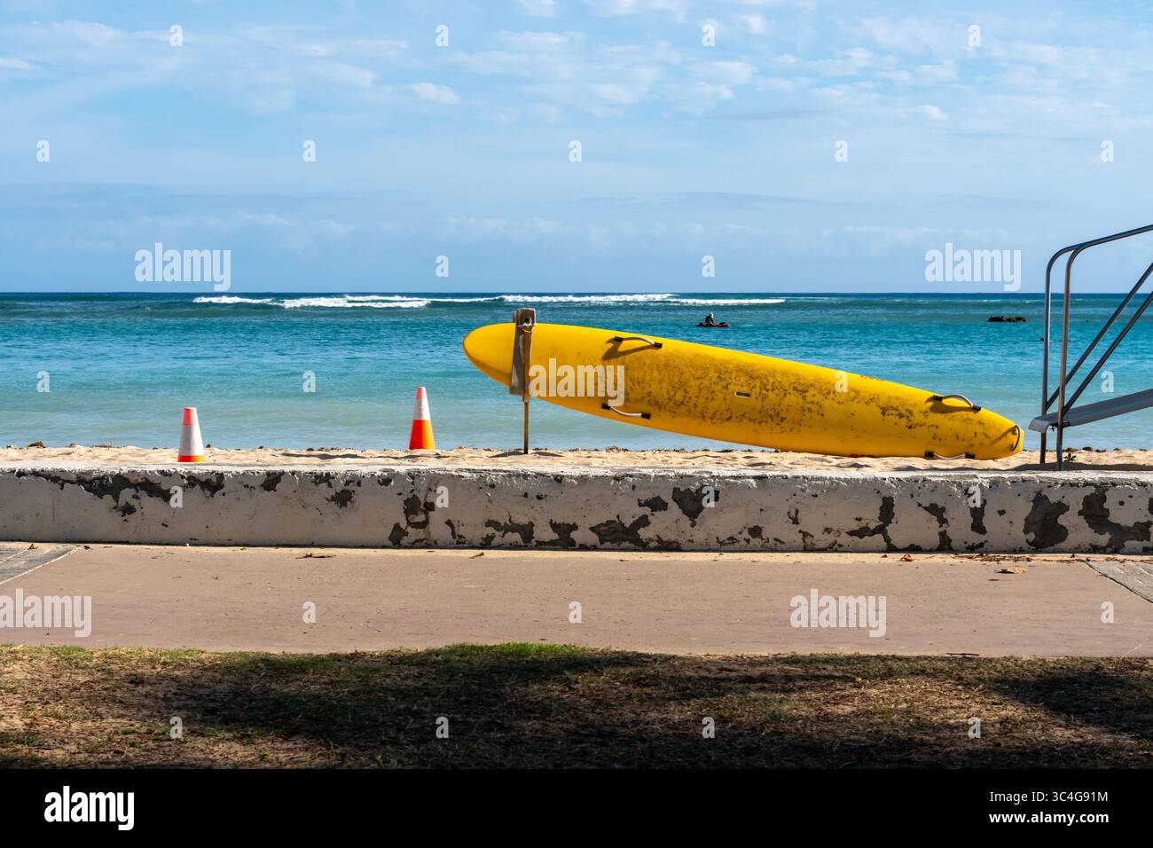 La planche de surf Yellow Lifeguard Rescue repose sur une plage tranquille, symbolisant la sécurité et la vigilance dans un ciel calme d'été avec le bord de l'océan en vue Banque D'Images