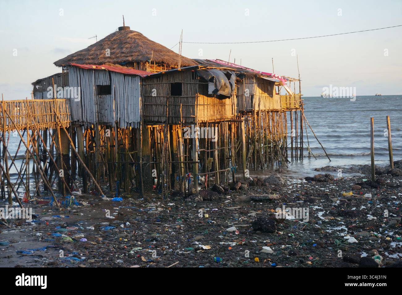 Restaurant Obama sur pilotis au-dessus de l'eau, mais beaucoup de déchets sales autour à marée basse. Soirée. Conakry, Guinée. Banque D'Images