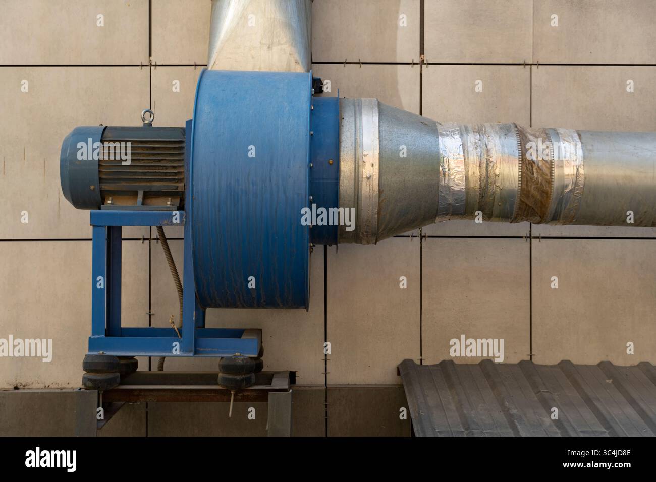 Gros plan de l'équipement de ventilation industrielle avec moteur bleu, gaines métalliques et fond de mur en béton Banque D'Images