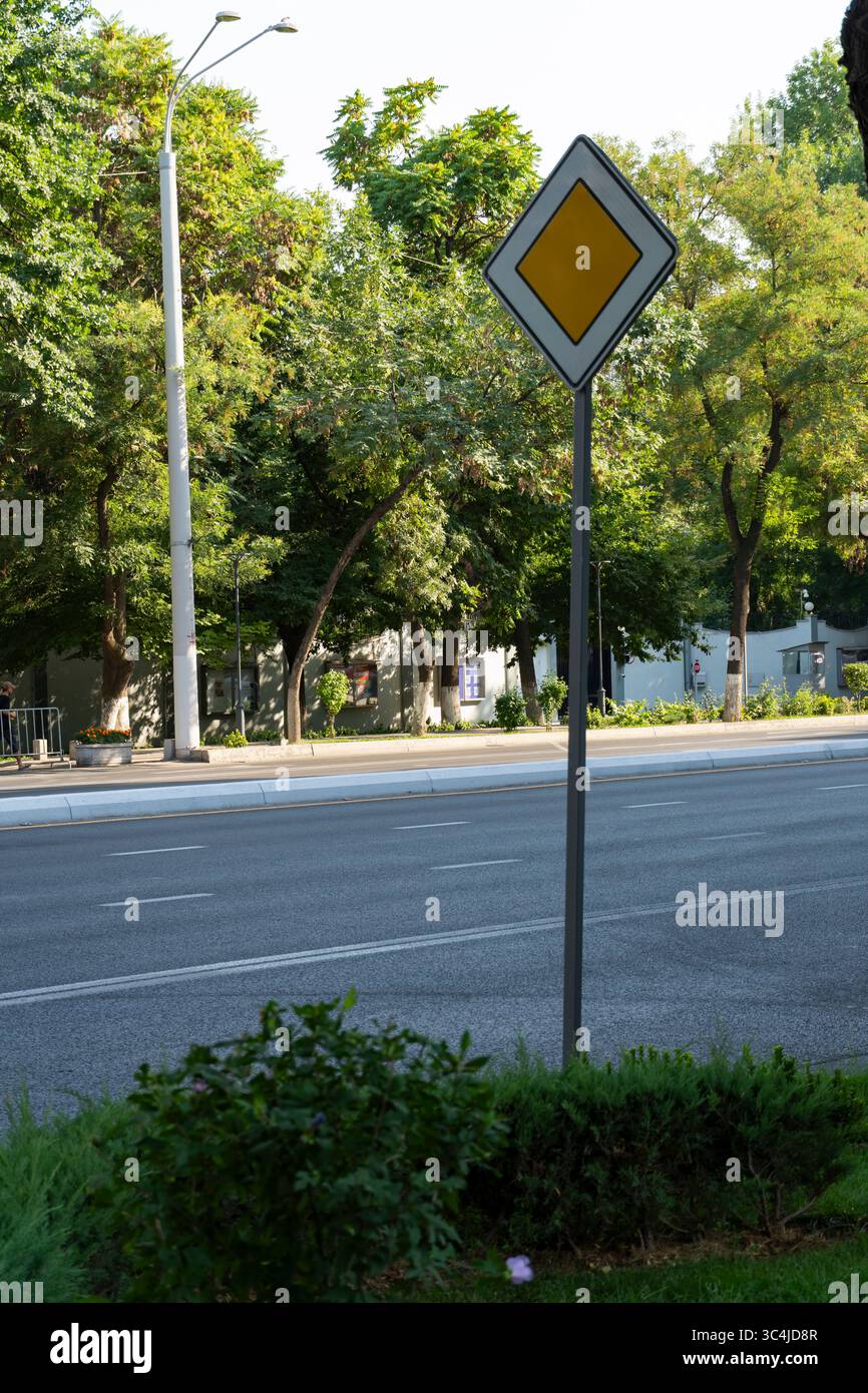 Un panneau routier prioritaire sur une rue sereine bordée d'arbres indique l'emprise des véhicules Banque D'Images