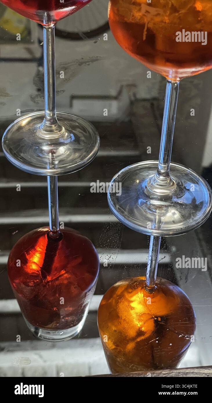 Des verres remplis de cocktails vibrants reposent sur une surface réfléchissante, créant des images en miroir. Les riches teintes rouge et ambre contrastent magnifiquement, aigu Banque D'Images Des verres remplis de cocktails vibrants reposent sur une surface réfléchissante, créant des images en miroir. Les riches teintes rouge et ambre contrastent magnifiquement, aigu Banque D'Images