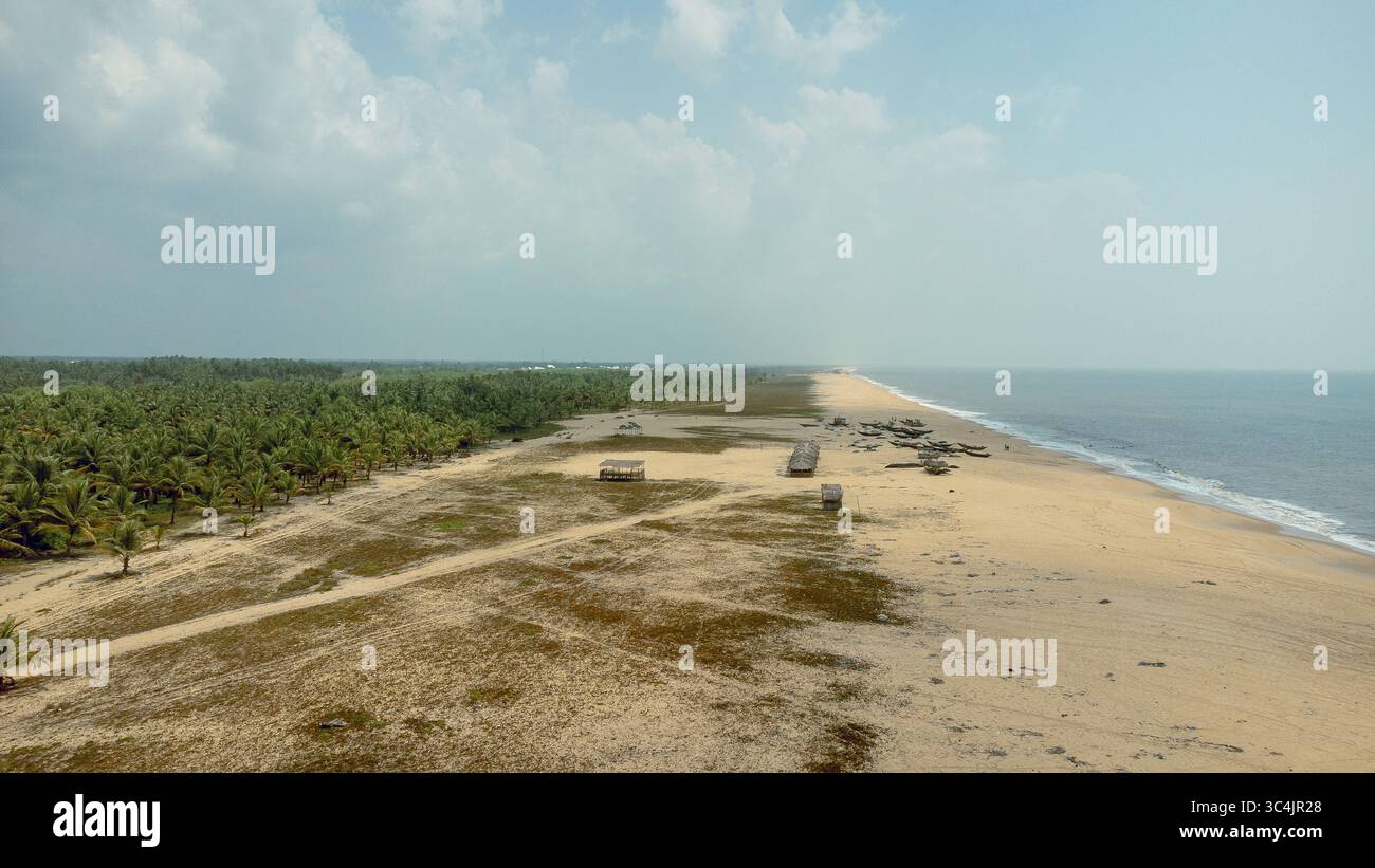 Vue aérienne des sables ensoleillés rencontrent la mer Azur, bordée d'arbres verdoyants et de cabanes dispersées sous un vaste ciel, Igbokoda, Ondo, Nigeria. Banque D'Images