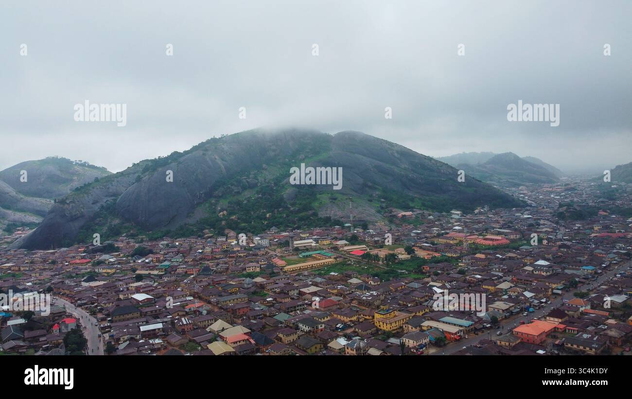 Vue aérienne d'un vaste paysage urbain niché sous une montagne majestueuse voilée dans la brume, où la vie urbaine rencontre la grandeur de la nature, Akure, Ondo, Nigeria. Banque D'Images
