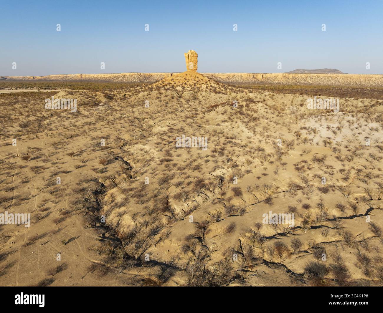Vue aérienne du paysage sombre et ensoleillé où une imposante formation rocheuse s'élève de la terre sèche, gravée d'ombres et de végétation desséchée, Da Banque D'Images