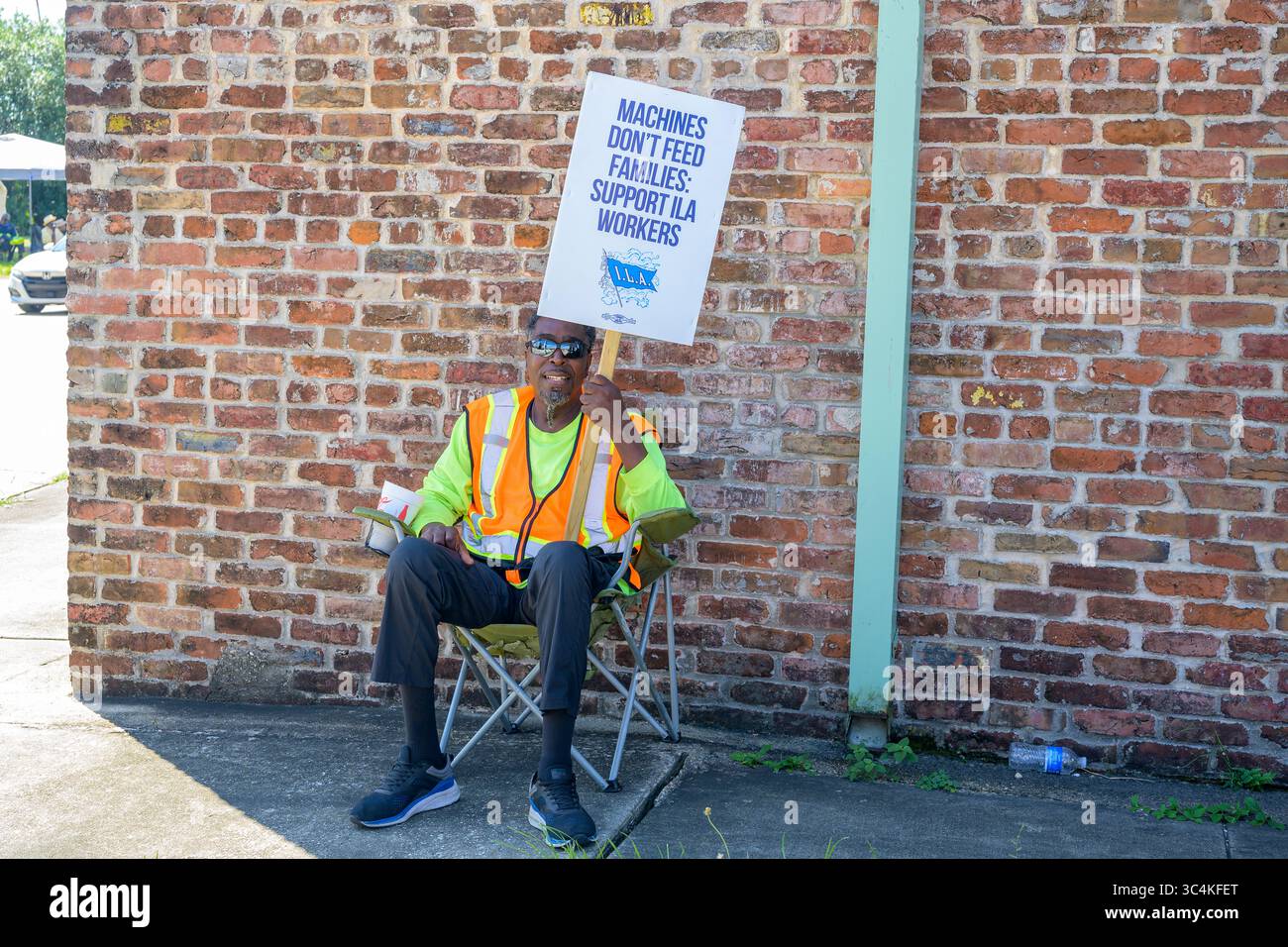 LA NOUVELLE-ORLÉANS, LOUISIANE, États-Unis - 2 OCTOBRE 2024 : un travailleur portuaire en grève, de l'Association internationale des débardeurs, est assis sur le trottoir avec un panneau de piquetage près de l'entrée du port de la Nouvelle-Orléans Banque D'Images