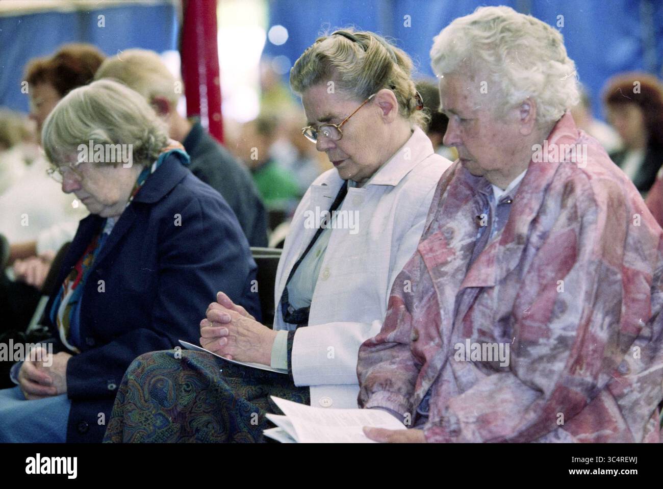 Evangelical meeting day, Velsen, Velsen, 31-05-1998 Whizgle News, Dutch Desk, pays-Bas, 1950-2000 trois femmes sont assises étroitement ensemble, chacune avec la tête inclinée dans la contemplation. Ils sont habillés de vêtements modestes et tiennent des papiers dans leurs mains. L'atmosphère suggère un moment de réflexion ou de prière, car ils semblent concentrés et sereins au milieu d'un rassemblement de personnes en arrière-plan. Banque D'Images