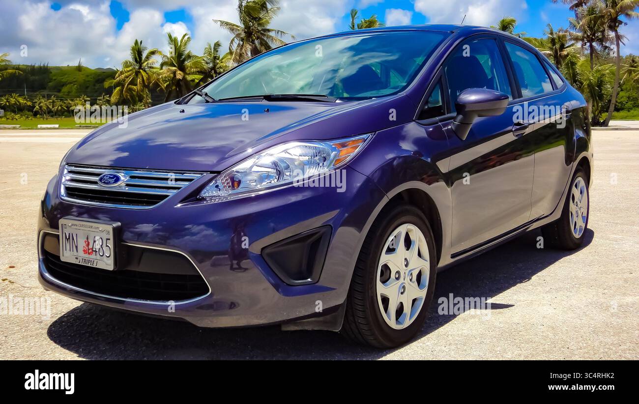 Une Ford Fiesta bleue garée sur une plage hawaïenne ensoleillée, encadrée par des palmiers - une voiture compacte joyeuse parfaite pour une escapade sur une île tropicale. Banque D'Images
