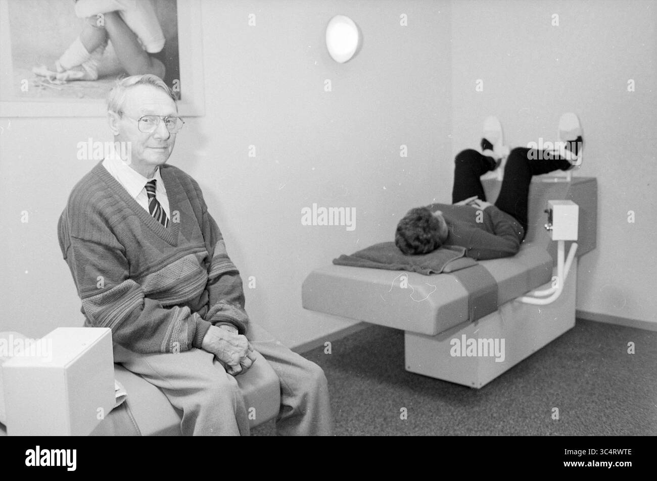 Centre sportif Santpoort pour patients atteints de rhumatisme, Sports et semaine sportive, Santpoort, 23-02-1989 Whizgle News, Dutch Desk, pays-Bas, 1950-2000 Un homme en costume et cravate s'assoit calmement sur un banc, observant un individu détendu allongé sur une table de traitement, éventuellement en cours d'intervention thérapeutique dans un cadre clinique. Banque D'Images