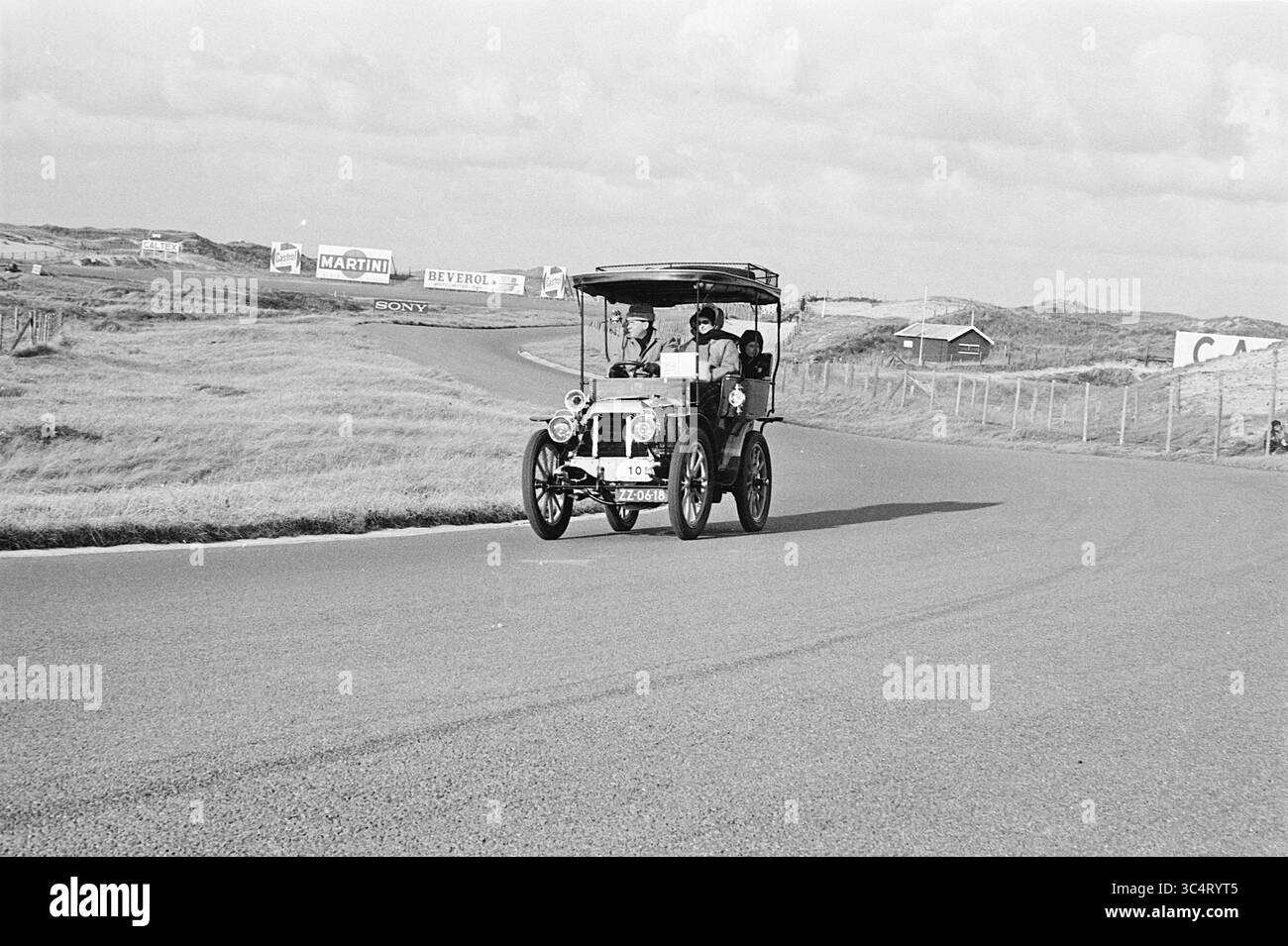 P.A.C. Ride on Zandvoort, Zandvoort, 13-10-1963 Whizgle News, Dutch Desk, pays-Bas, 1950-2000 une automobile du début du XXe siècle roule le long d'une route sinueuse, avec de vastes champs herbeux et des panneaux publicitaires lointains en arrière-plan. La voiture, avec un design vintage distinct, met en valeur le charme d'une époque révolue en naviguant sur la piste. Banque D'Images