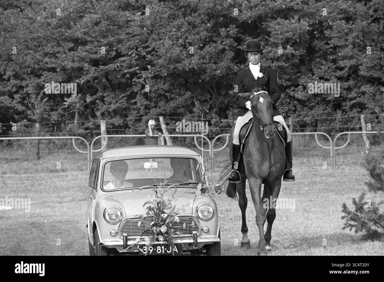 A. Ebben, lauréat MB, concours, 02-08-1969 Whizgle News, Dutch Desk, pays-Bas, 1950-2000 Un cavalier en tenue formelle est gracieusement assis au sommet d'un cheval, tandis qu'une voiture classique ornée de décorations florales est garée à proximité. La scène se déroule dans un champ verdoyant et luxuriant, entouré d'arbres et d'un spectateur lointain. Banque D'Images
