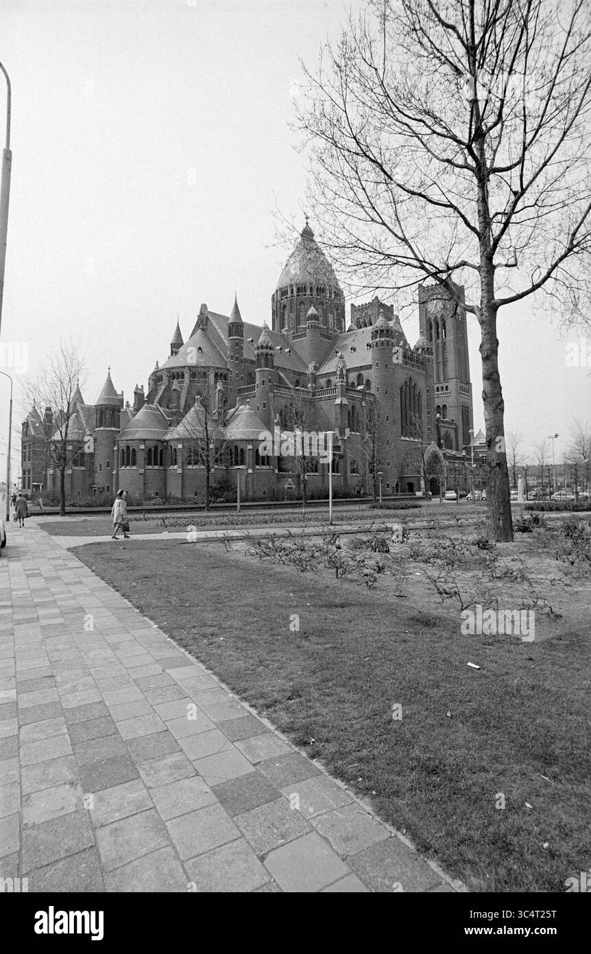 Extérieur de la basilique de Bavo Haarlem on the Leidsevaart, Exterior, Haarlem, Leidsevaart, pays-Bas, 28-04-1973 Whizgle News, Dutch Desk, pays-Bas, 1950-2000 Un grand bâtiment orné de détails architecturaux complexes, entouré d'un espace paysager avec des allées et des arbres. La structure présente un mélange de tours et de toits uniques, créant une présence visuelle saisissante. Une figure solitaire marche le long du sentier, soulignant l'échelle de l'édifice. Banque D'Images