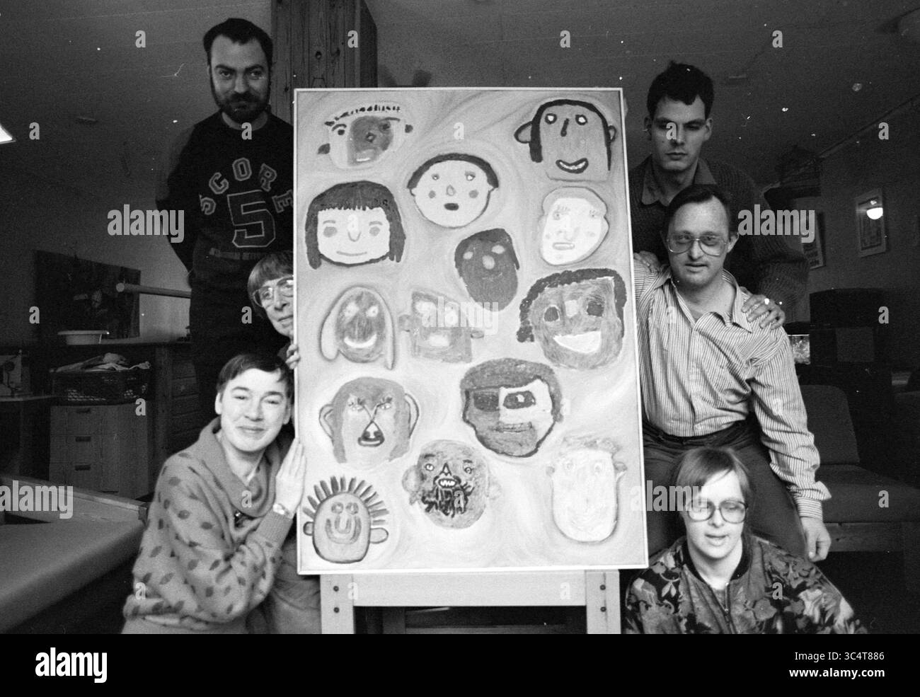 Personnes handicapées avec peinture, Haarlem, pays-Bas, 24-01-1991 Whizgle News, Dutch Desk, pays-Bas, 1950-2000 Un groupe d'individus se tient debout et s'agenouille autour d'une grande toile affichant un éventail de visages colorés, reflétant une variété d'émotions et d'expressions. La scène capture un moment de collaboration et de créativité, mettant en valeur les divers styles artistiques des participants. Banque D'Images