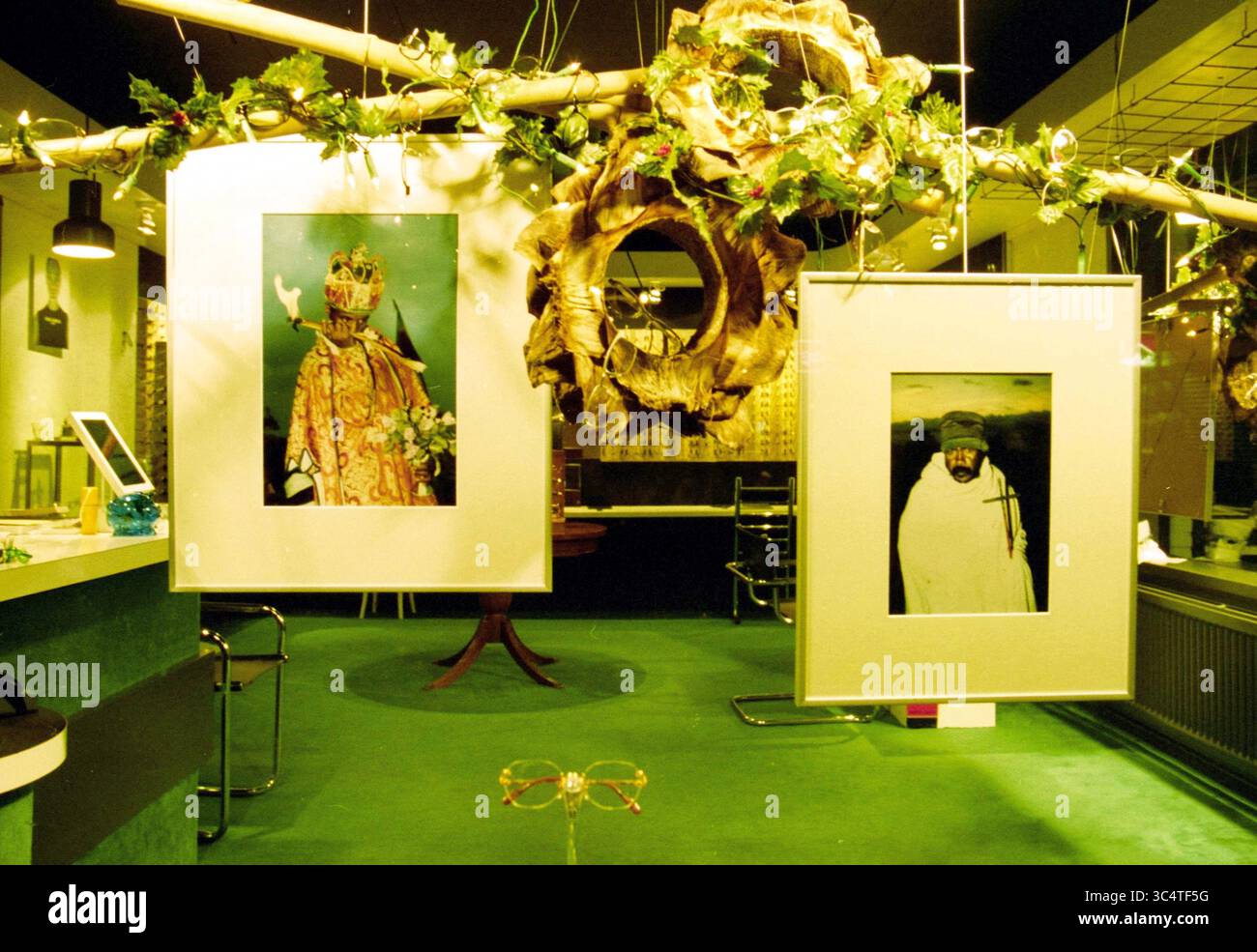Vitrine, Santpoort, Santpoort, 04-12-2000 Whizgle News, Dutch Desk, pays-Bas, 1950-2000 la scène présente un espace galerie contemporain orné de tapis vert éclatant et de feuillage suspendu. Deux portraits encadrés de premier plan présentent des personnages dans une tenue élaborée, évoquant un sens de l'importance culturelle. L'arrangement attire l'œil sur un mélange éclectique d'éléments décoratifs, y compris une couronne circulaire et des meubles élégants, créant une atmosphère unique d'expression artistique. Banque D'Images