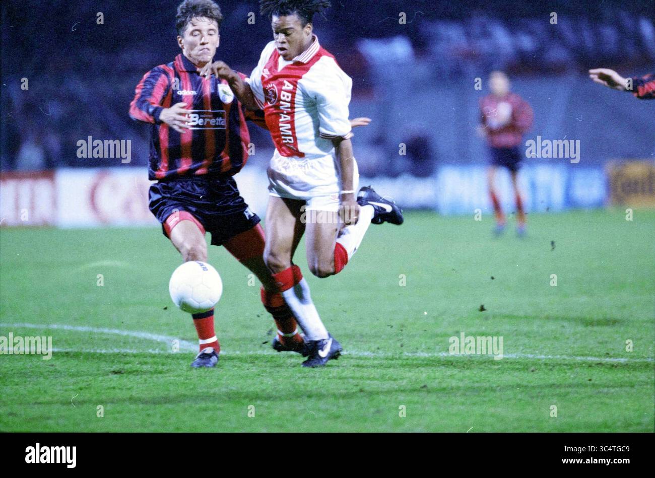 Football, Ajax - Grasshopper, 17-10-1995 Whizgle News, Dutch Desk, pays-Bas, 1950-2000 deux joueurs de football sont engagés dans un match de compétition, rivalisant pour le contrôle du ballon. Un joueur, portant un uniforme rayé rouge et noir, tente de défier l'autre, qui porte une tenue majoritairement blanche. L'action est intense alors qu'ils naviguent sur le terrain herbeux, entouré par un fond de fans et de lumières de stade. Banque D'Images