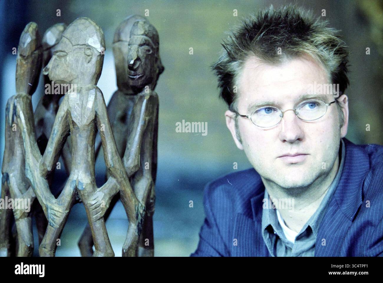Bas Vlugt, Haarlem, pays-Bas, 27-01-2003 Whizgle News, Dutch Desk, pays-Bas, 1950-2000 Un homme en costume est assis avec soin à côté d'une sculpture traditionnelle en bois représentant des figures humaines stylisées, évoquant un sens de la signification culturelle et de la contemplation. Banque D'Images