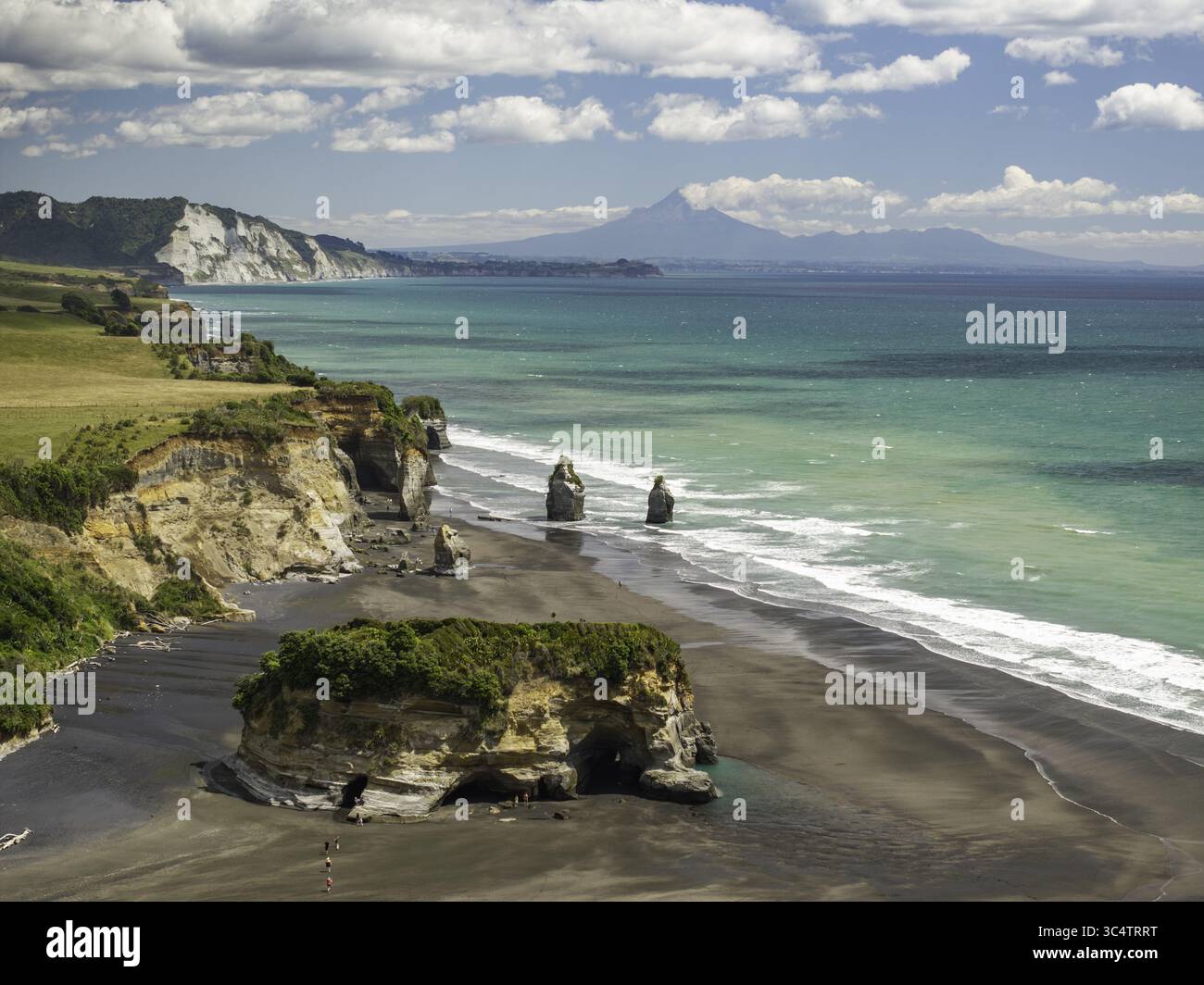 Vue aérienne du paysage côtier spectaculaire où le sable noir rencontre les eaux turquoises, encadrée par la silhouette lointaine du mont Taranaki, New Plymout Banque D'Images