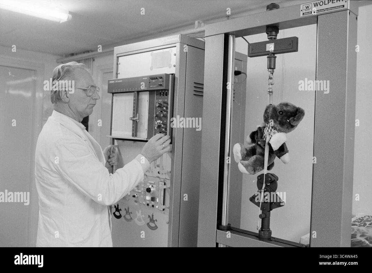 Inspection service d'inspection de jouets, inspections, Jeux et jouets, Haarlem, pays-Bas, 03-01-1985 Whizgle News, Dutch Desk, pays-Bas, 1950-2000 Un scientifique en blouse de laboratoire fait fonctionner une machine alors qu'un chien en peluche est suspendu à un appareil d'essai, mettant en évidence une expérience dans l'essai de matériaux ou de produits. Banque D'Images