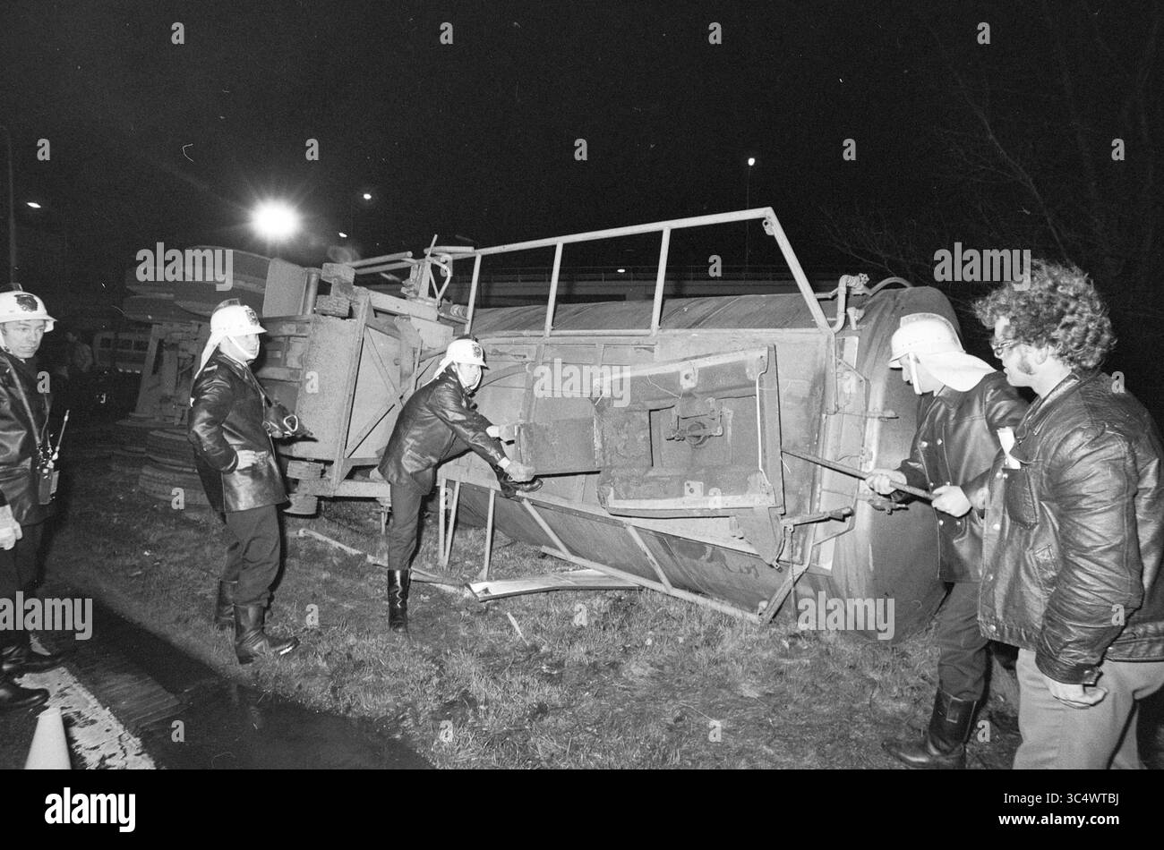 Accident camion-citerne d'acide nitrique, accidents, collisions, accidents, 18-01-1974 Whizgle News, Dutch Desk, pays-Bas, 1950-2000 les intervenants d'urgence examinent un véhicule renversé, avec des membres d'équipage en équipement de protection évaluant la situation. La scène est éclairée par de la lumière artificielle, soulignant l'urgence de l'incident alors qu'ils travaillent pour faire face aux conséquences. Banque D'Images