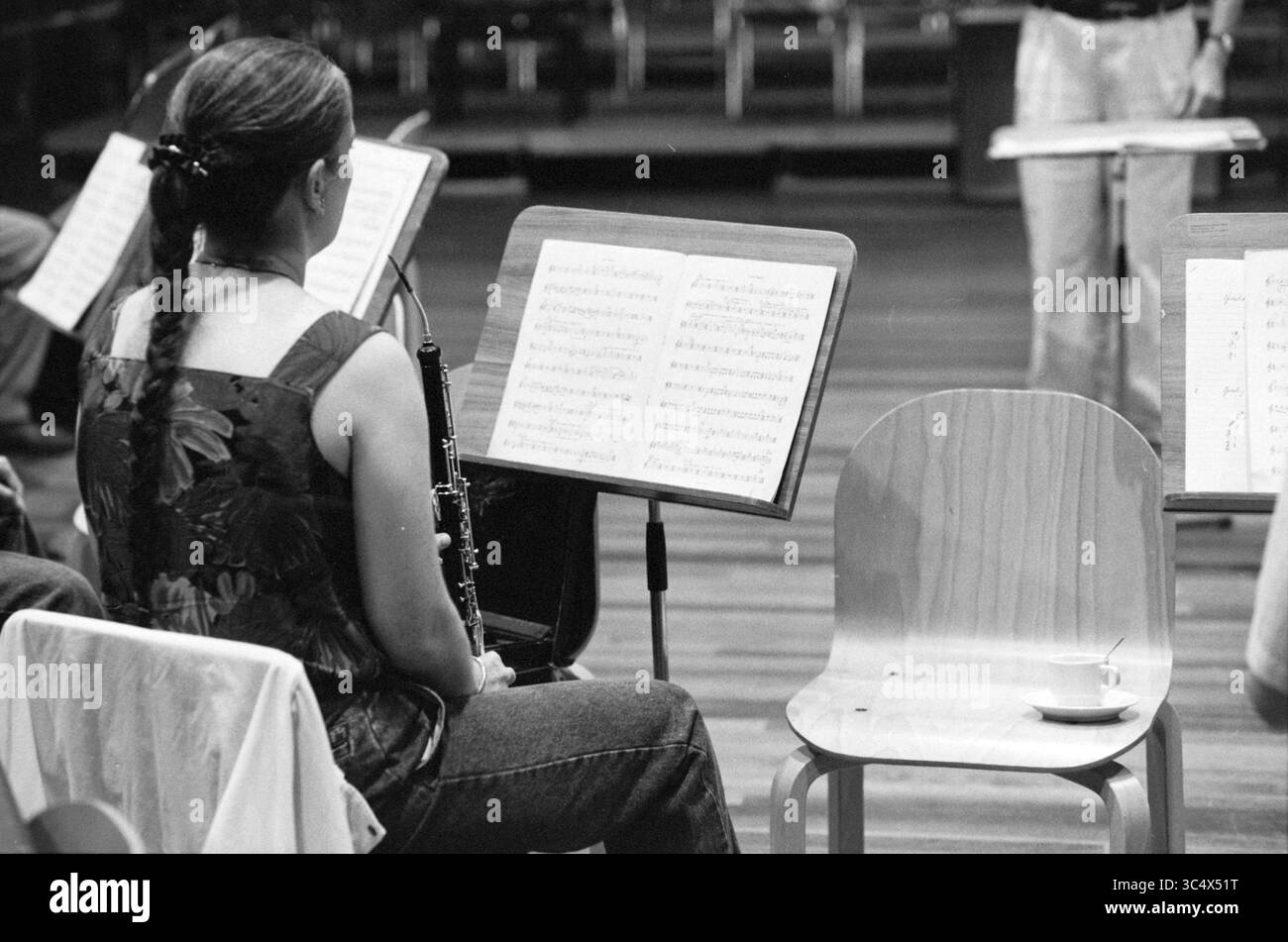 Rehearsal A.P.O., Amsterdam, pays-Bas, 14-08-1990 Whizgle News, Dutch Desk, pays-Bas, 1950-2000 Un musicien est assis attentivement avec une clarinette à la main, concentré sur la partition devant eux, tandis qu'une chaise vide à proximité tient une petite tasse, suggérant une pause dans la répétition. Banque D'Images