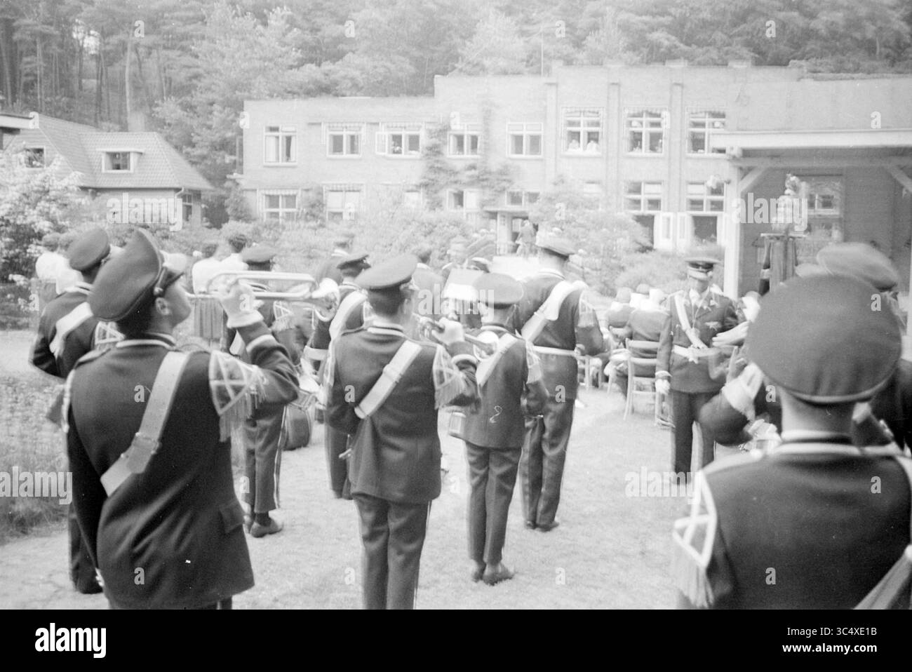 Interprétation par le groupe de musique 'Musiekvereniging NZH' dans un domicile ou un hôpital, Bloemendaal, Bergweg Whizgle News, Dutch Desk, pays-Bas, 1950-2000 Une fanfare vêtue d'uniformes formels joue des instruments alors qu'ils défilent à travers un rassemblement, avec en toile de fond des bâtiments et des arbres. L'atmosphère évoque une occasion cérémonielle ou festive, mettant en évidence la fierté et l'unité de l'organisation. Banque D'Images
