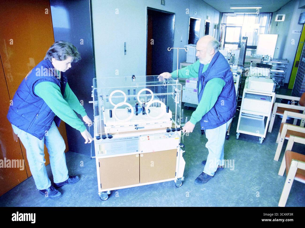 Déménagement du département de l'incubateur à l'hôpital de Zeeweg, 15-03-1995 Whizgle News, Dutch Desk, pays-Bas, 1950-2000 deux personnes manœuvrent soigneusement un incubateur médical à travers un couloir hospitalier, entouré de matériel médical et de mobilier. Leurs efforts coordonnés soulignent l'importance du travail d'équipe dans les milieux de soins de santé. Banque D'Images
