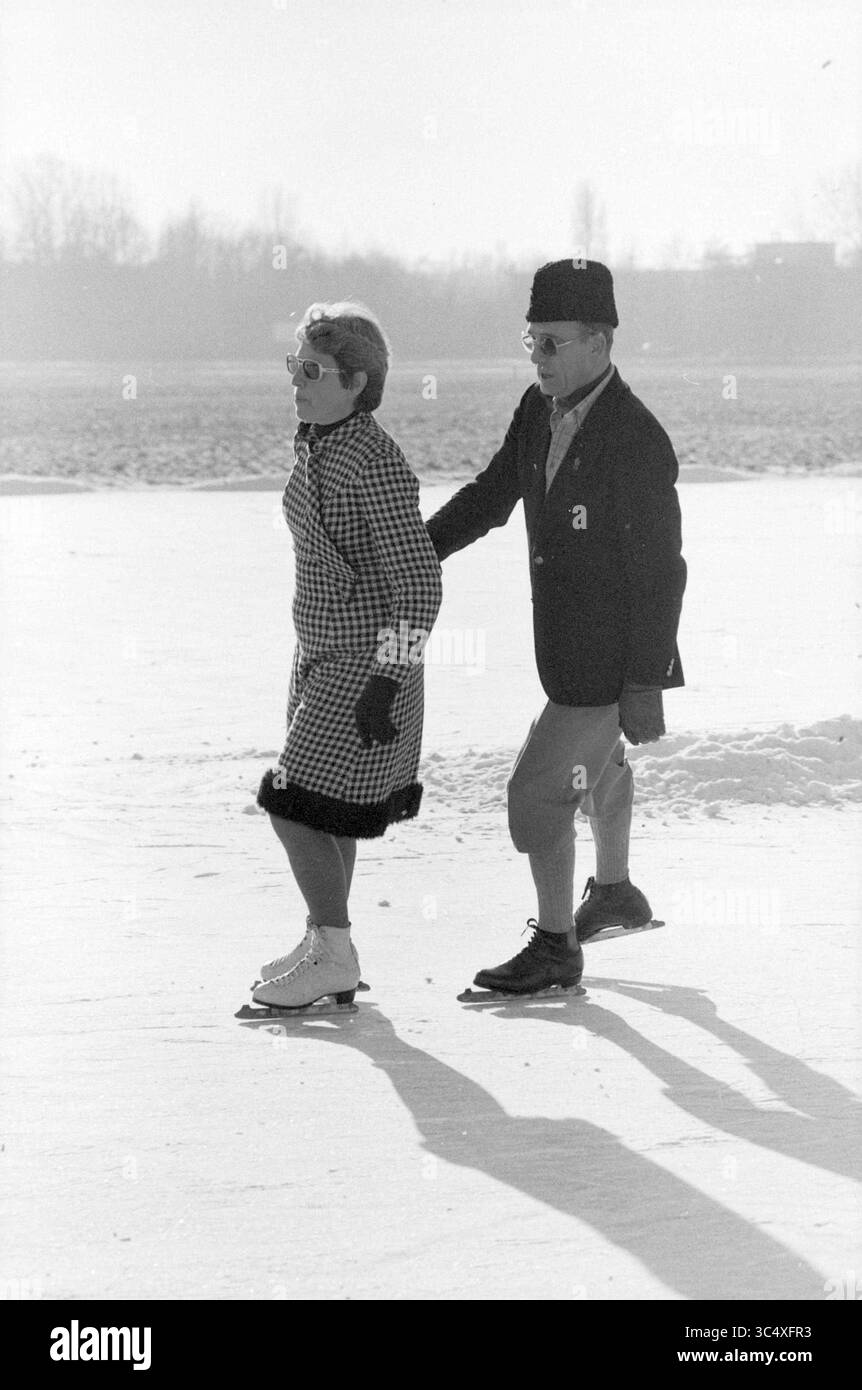 Nettoyage de la patinoire Ouderkerk aan de Amstel, patinage, glace, patinoire, hockey sur glace, Ouderkerk aan de Amstel, 14-01-1982 Whizgle News, Dutch Desk, pays-Bas, 1950-2000 Un couple glisse gracieusement sur une surface glacée, vêtu d'une élégante tenue d'hiver. La femme arbore un manteau à motifs et des lunettes de soleil, tandis que l'homme, portant un chapeau et une veste sur mesure, l'assiste lorsqu'ils patinent ensemble. Les ombres s'étendent sous eux, capturant l'atmosphère sereine d'une journée d'hiver. Banque D'Images