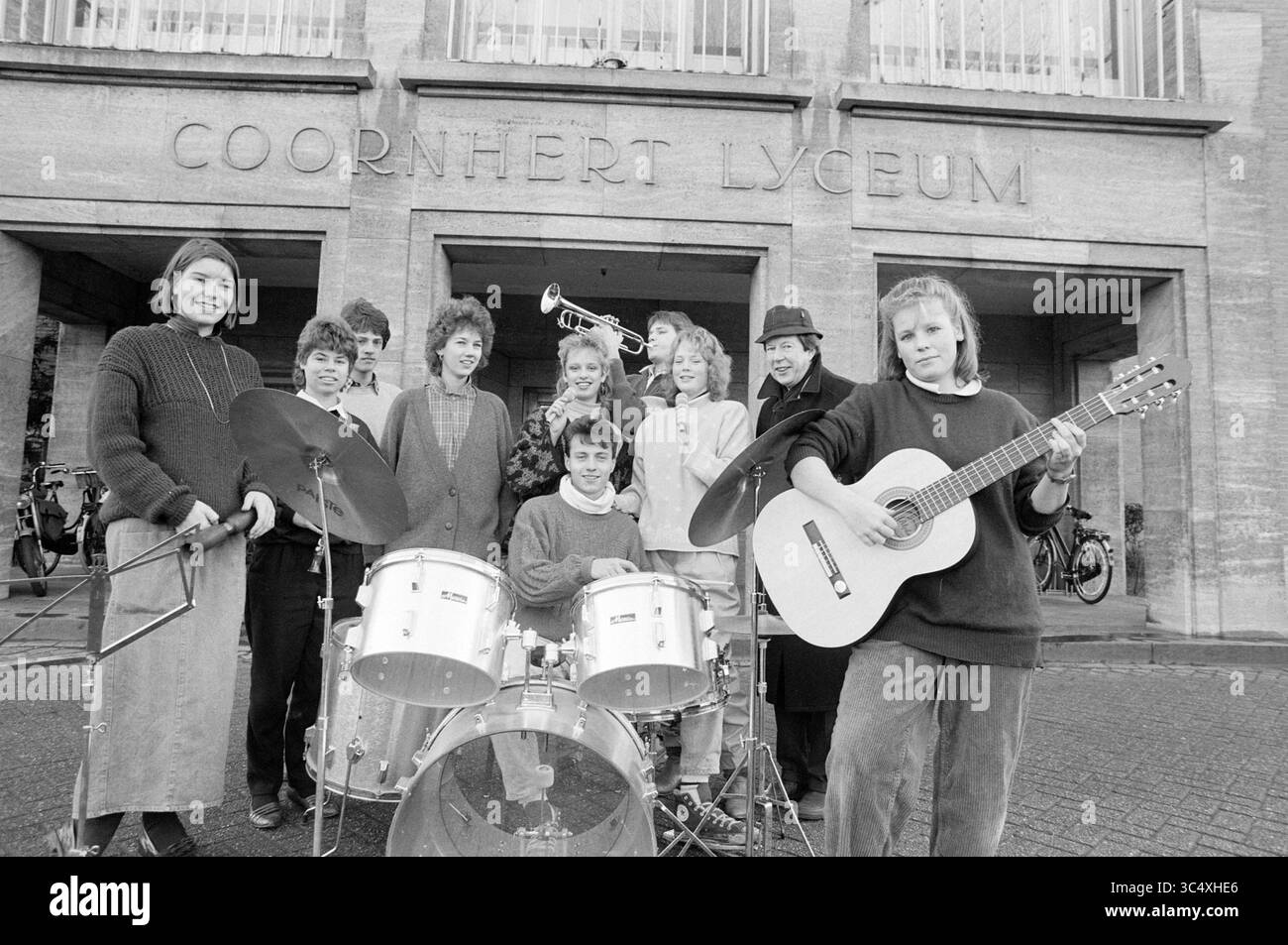 Étudiants en musique Coornhert Lyceum, 27-01-1987 Whizgle News, Dutch Desk, pays-Bas, 1950-2000 Un groupe animé de musiciens se réunit à l'extérieur d'une école, présentant une variété d'instruments, dont la batterie, une trompette et une guitare. Ils portent des vêtements décontractés et affichent un sentiment de camaraderie et d'enthousiasme, posant ensemble devant l'entrée d'un bâtiment emblématique. Banque D'Images