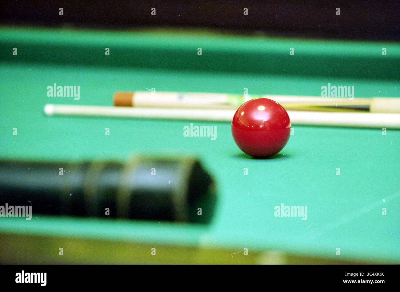 Billard : P. Adrichem, Santpoort, Santpoort, 13-10-1998 Whizgle News, Dutch Desk, pays-Bas, 1950-2000 Une boule de billard rouge éclatante repose sur une table en feutre vert, entourée de bâtons de queue et du bord flou d'une pointe de queue, invitant à un jeu d'adresse et de stratégie. Banque D'Images