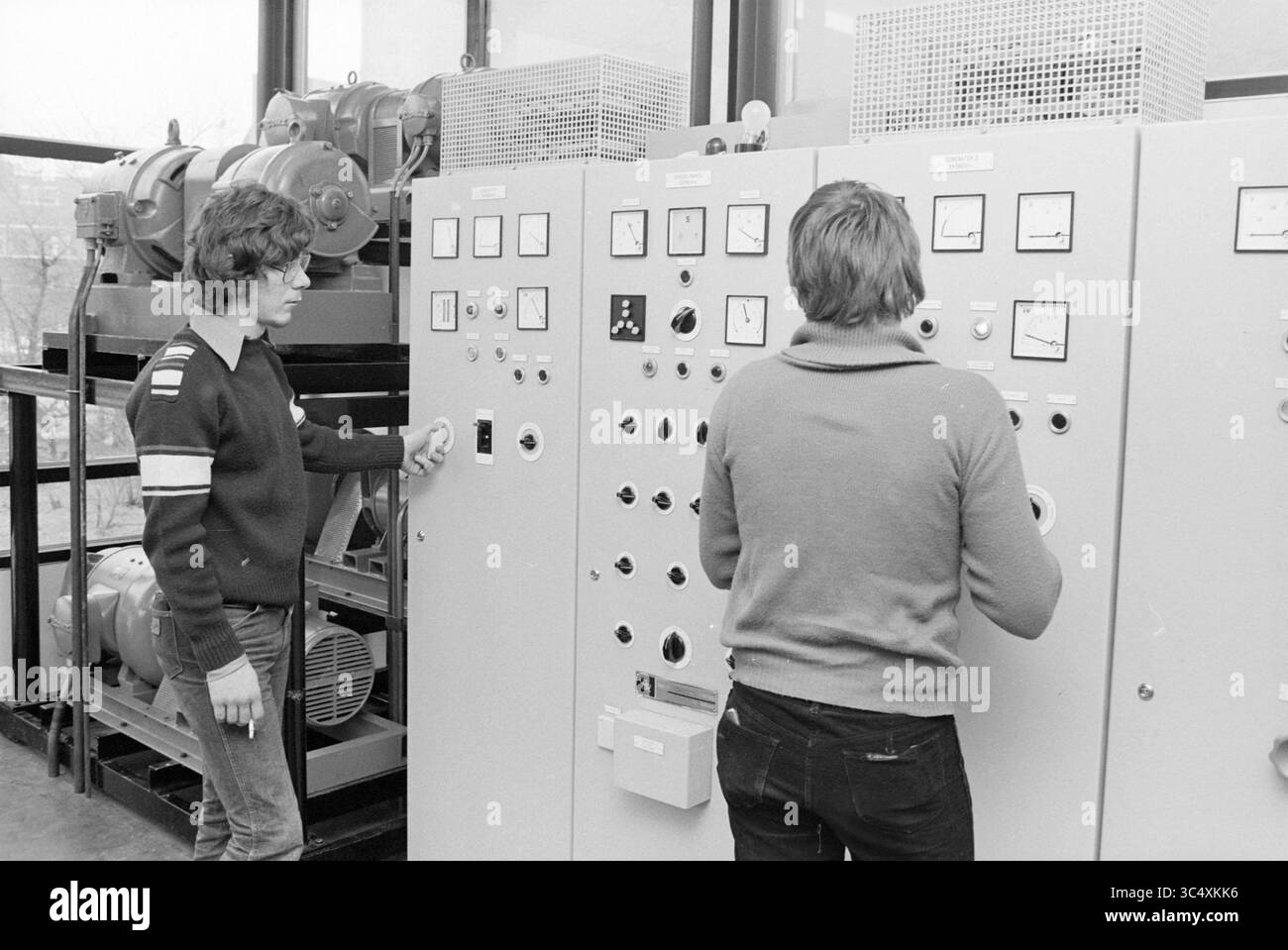 Panneau de commande de moteur marin, École maritime, IJm., construction navale, expédition, IJmuiden, pays-Bas, 23-02-1979 Whizgle News, Dutch Desk, pays-Bas, 1950-2000 deux personnes se concentrent sur un panneau de commande rempli de divers cadrans, interrupteurs et jauges. Une personne règle activement une commande tandis que l'autre surveille les lectures, entourée de machines dans un cadre technique. Banque D'Images