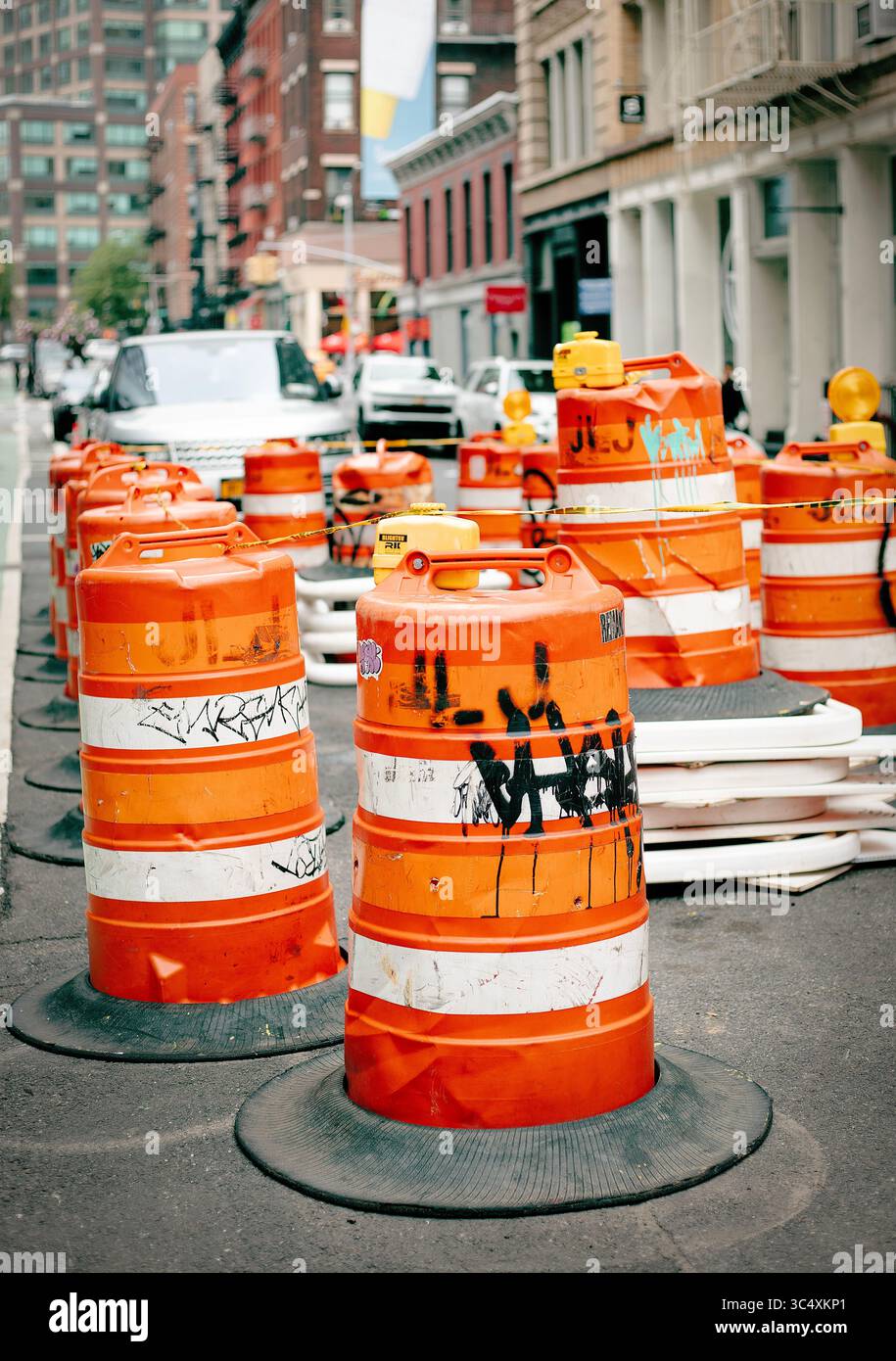Des barils de circulation orange bordent une rue urbaine animée, guidant les véhicules à travers une zone de construction à New York City, NY, USA le 16 mai 2025. Banque D'Images