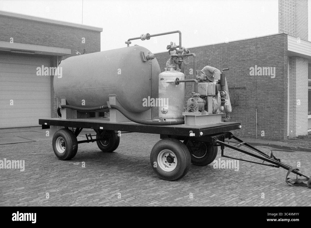 Portrait de l'entreprise Sihi Martens usine de pompes Beverwijk, installations de pompes, Beverwijk, pays-Bas, 25-01-1983 Whizgle News, Dutch Desk, pays-Bas, 1950-2000 Un grand réservoir cylindrique monté sur une plate-forme à roues, avec divers composants mécaniques et tuyaux, indicatif d'un équipement industriel. Une personne est vue en train de faire fonctionner ou inspecter la machine. Banque D'Images
