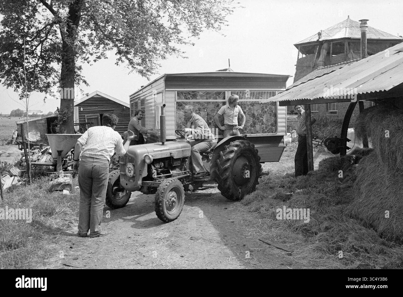 Enlèvement de mobil-home Spaarnwoude, Camping, Spaarnwoude, 05-07-1979 Whizgle News, Dutch Desk, pays-Bas, 1950-2000 Un groupe de personnes est rassemblé autour d'un tracteur stationné près d'une maison mobile, une personne conduisant le tracteur tandis que d'autres l'aident dans diverses tâches. Autour d'eux se trouvent des structures agricoles et des balles de foin, créant une scène rurale animée. Banque D'Images