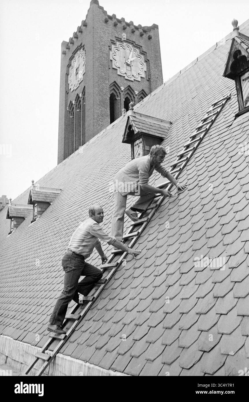 Monument Guard, Haarlem, monuments, 21-07-1982 Whizgle News, Dutch Desk, pays-Bas, 1950-2000 deux hommes grimpent un toit escarpé en utilisant des échelles, travaillant sur les bardeaux d'ardoise. En arrière-plan, une grande tour d'horloge avec un cadran décoratif se tient en évidence. La scène suggère des travaux d'entretien ou de réparation en cours sur le bâtiment. Banque D'Images