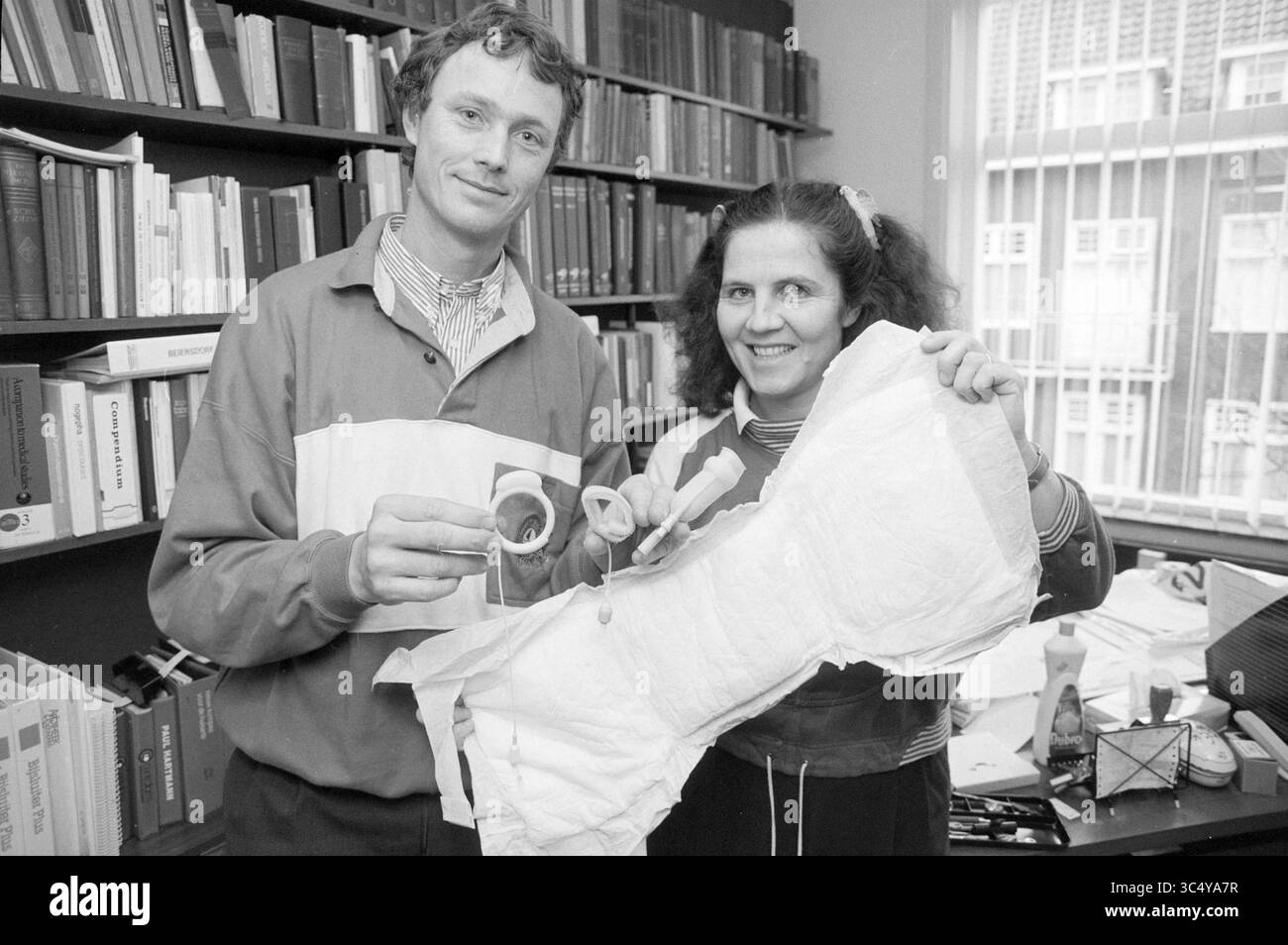 Un homme et une femme dans une étude montrent une très grande couche, 11-11-1993 Whizgle News, Dutch Desk, pays-Bas, 1950-2000 deux individus sourient et tiennent un morceau de tissu ou de matériau, l'un affichant un petit objet rond. Ils semblent être dans un cadre universitaire ou de recherche, entourés d’étagères de livres et de papiers, suggérant un projet collaboratif ou une présentation liée aux textiles ou aux matériaux. Banque D'Images