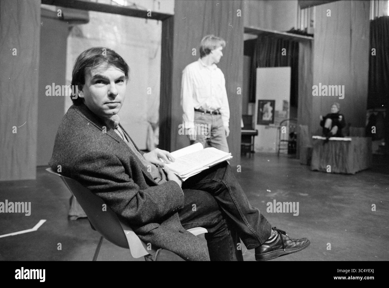 Réalisateur Babicki, Haarlems Toneel, 14-02-1996 Whizgle News, Dutch Desk, pays-Bas, 1950-2000 Un homme est assis sur une chaise, tenant intentionnellement un script tout en observant une répétition qui se déroule sur une scène de théâtre. En arrière-plan, deux acteurs sont engagés dans une scène, contribuant à l'atmosphère créative de l'espace. Banque D'Images