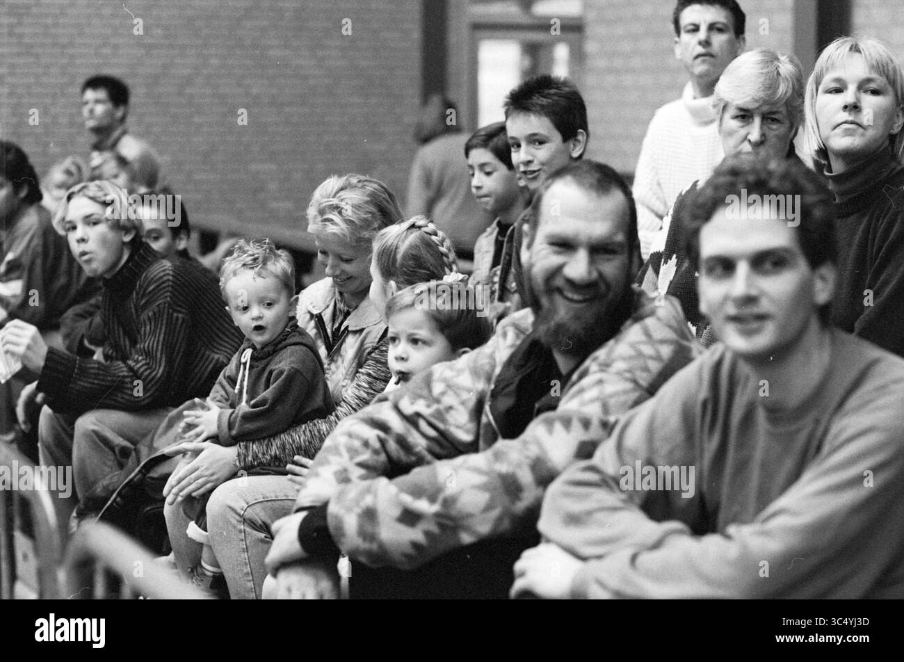 Audience aux équipes de rue du tournoi de football en salle, Velserbroek, 17-01-1997 Whizgle News, Dutch Desk, pays-Bas, 1950-2000 Un groupe de personnes diverses, y compris des enfants et des adultes, s'assoient étroitement ensemble, manifestant un éventail d'expressions allant de la curiosité au contentement. La scène capture un moment d’expérience partagée, probablement dans un cadre communautaire ou social. Banque D'Images