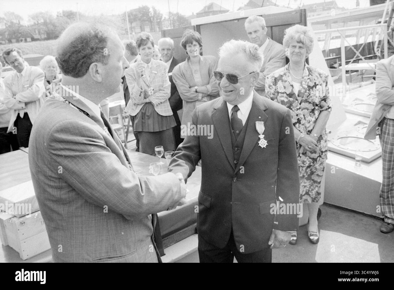 Pourrait. Prix Mr. Koppe, K.V.S.A., Royal Honors, 26-05-1989 Whizgle News, Dutch Desk, pays-Bas, 1950-2000 Un rassemblement formel avec un échange de salutations entre deux hommes, dont l'un est orné d'une médaille. Plusieurs spectateurs, vêtus de vêtements variés, observent l'interaction avec intérêt, suggérant un moment de célébration ou de reconnaissance. Banque D'Images