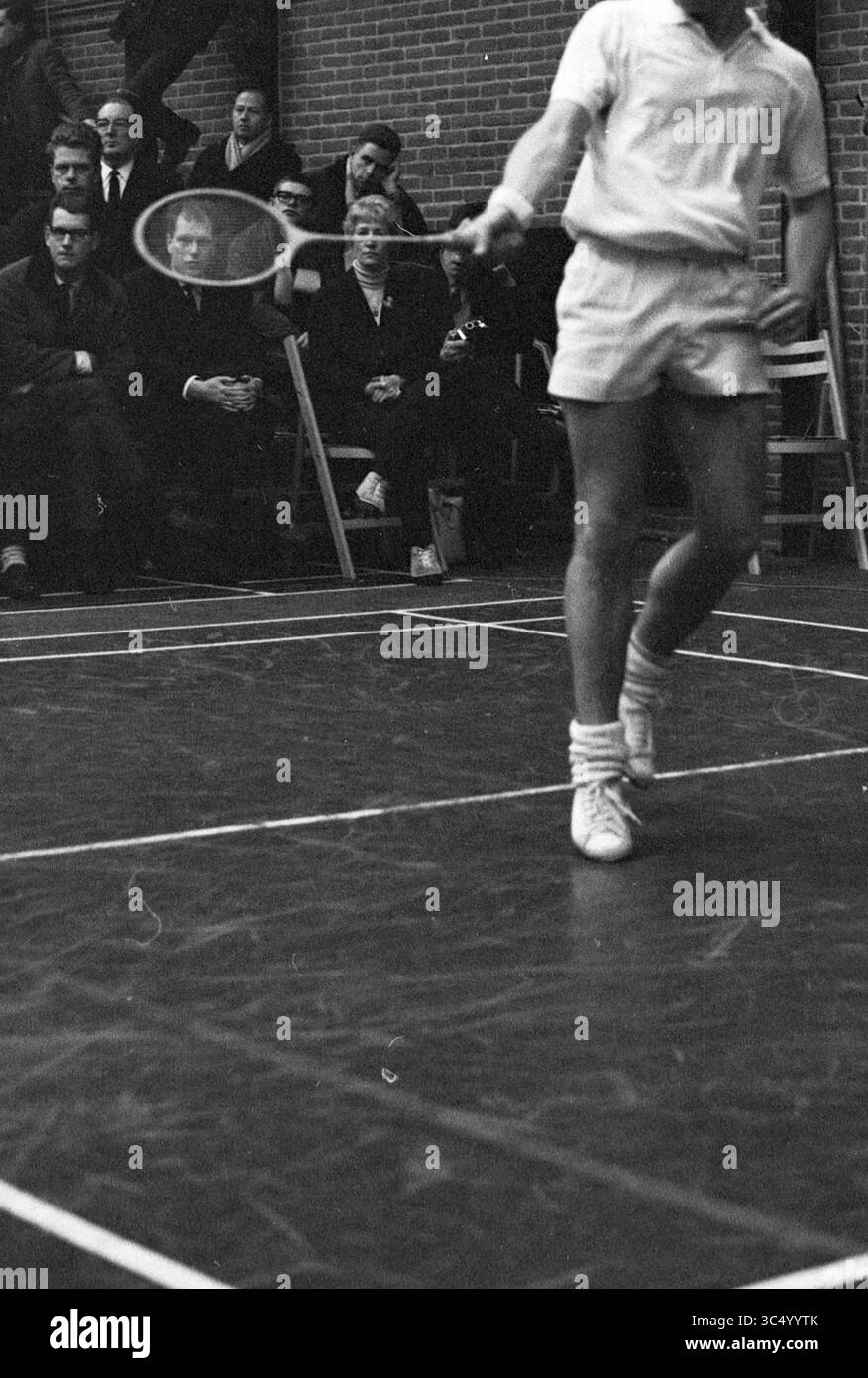 Badminton dans le Duinwijckhal du club de badminton Duinwijck, Haarlem, Badmintonpad, pays-Bas Whizgle News, Dutch Desk, pays-Bas, 1950-2000 joueur de tennis, à mi-swing avec une raquette, se concentre intensément sur le jeu tandis que les spectateurs regardent depuis les lignes de touche, certains paraissant profondément dans la pensée. L'atmosphère est celle d'un vif intérêt et d'anticipation. Banque D'Images