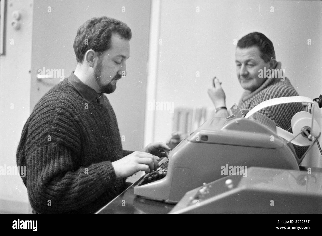 Mark Glotsbach, personnes, 19-03-1963 Whizgle News, Dutch Desk, pays-Bas, 1950-2000 deux hommes sont engagés dans un moment concentré à un bureau. Un homme tape intensément sur une machine à écrire, vêtu d'un pull confortable et épais, tandis que l'autre est assis à proximité, l'air amusé, avec une cigarette à la main. Le cadre semble décontracté mais déterminé, faisant allusion à une entreprise ou une conversation partagée. Banque D'Images