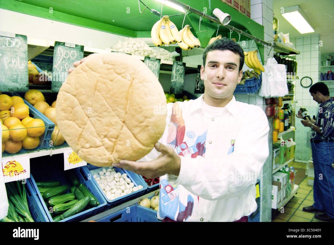 Pain marocain, marché au beurre, Haarlem, Botermarkt, pays-Bas, 07-08-1996 Whizgle News, Dutch Desk, pays-Bas, 1950-2000 Un jeune homme tient fièrement un grand pain rond dans une épicerie animée remplie de produits frais, y compris des oranges et des bananes, mettant en valeur une atmosphère de marché animée. Banque D'Images