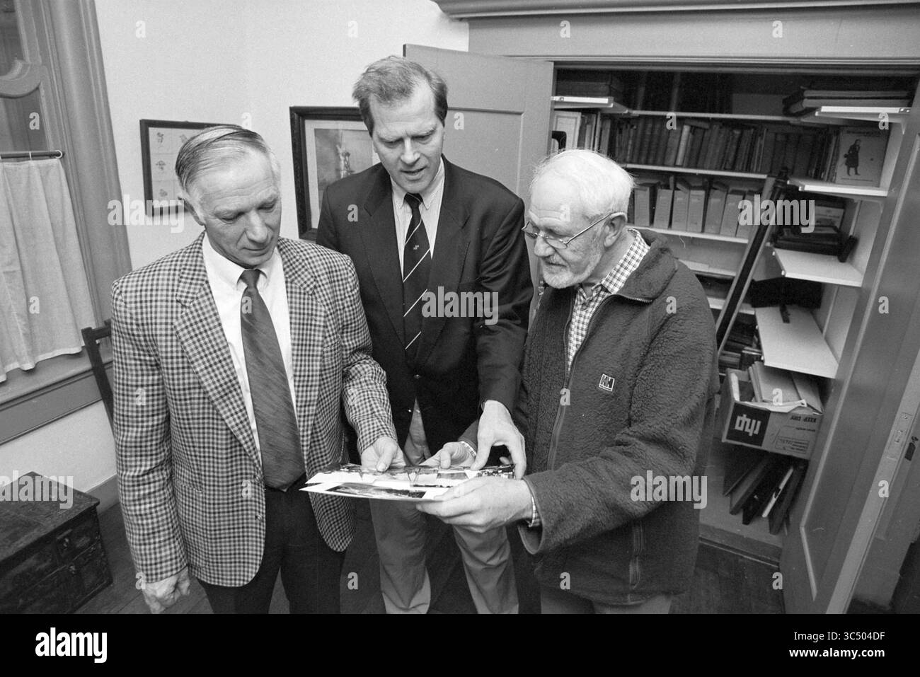 Trois messieurs avec de vieilles photos, Haarlem, pays-Bas, 26-10-1993 Whizgle News, Dutch Desk, pays-Bas, 1950-2000 trois hommes sont rassemblés, examinant une photographie de près. Leurs expressions véhiculent de l'intérêt et de l'engagement, et ils sont entourés d'étagères remplies de dossiers et d'images encadrées en arrière-plan. Le paramètre semble être un bureau ou un examen. Banque D'Images