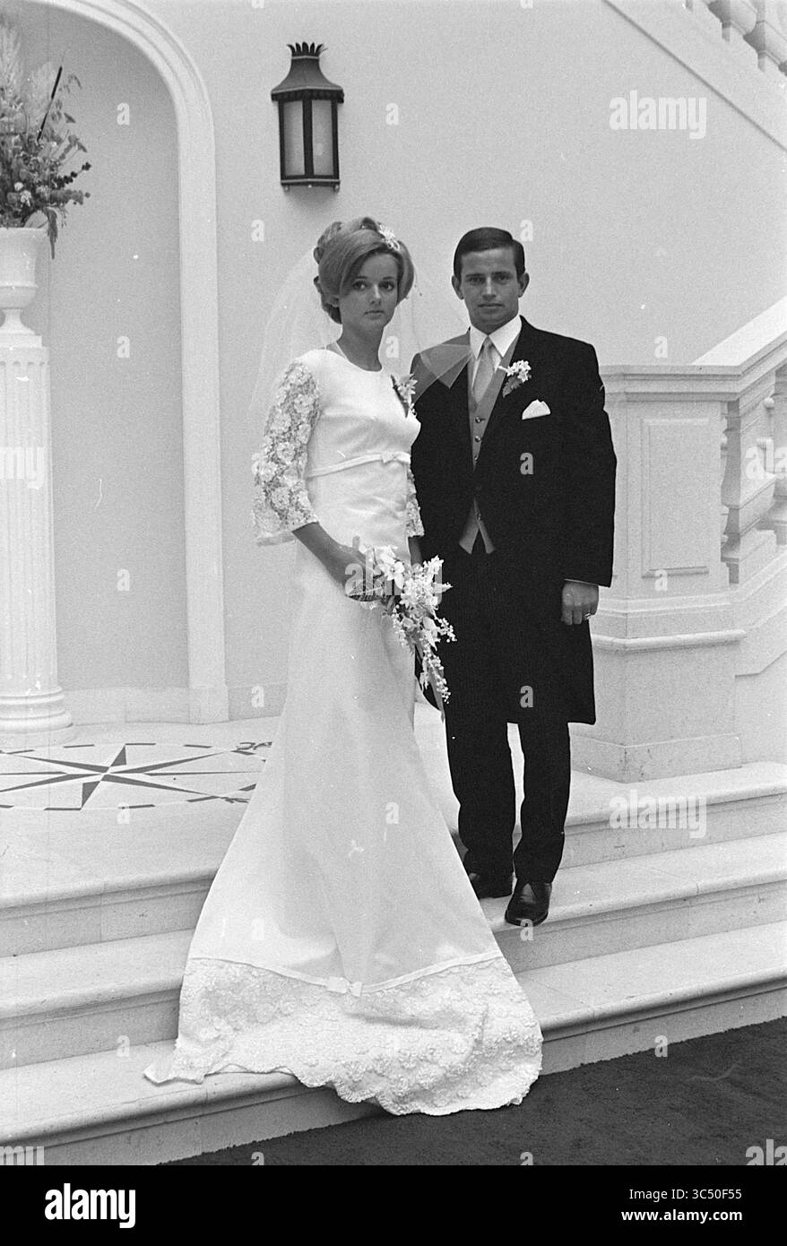 Mariage Frans v.d. Mountain, mariage, 19-09-1969 Whizgle News, Dutch Desk, pays-Bas, 1950-2000 Un couple se tient sur un grand escalier, élégamment habillé pour le jour de leur mariage. La mariée, portant une superbe robe avec des détails en dentelle et un voile, tient un bouquet de fleurs, tandis que le marié est nettement vêtu d'un costume classique avec une boutonnière. Ils posent avec confiance, incarnant un moment de célébration et d’amour. Banque D'Images